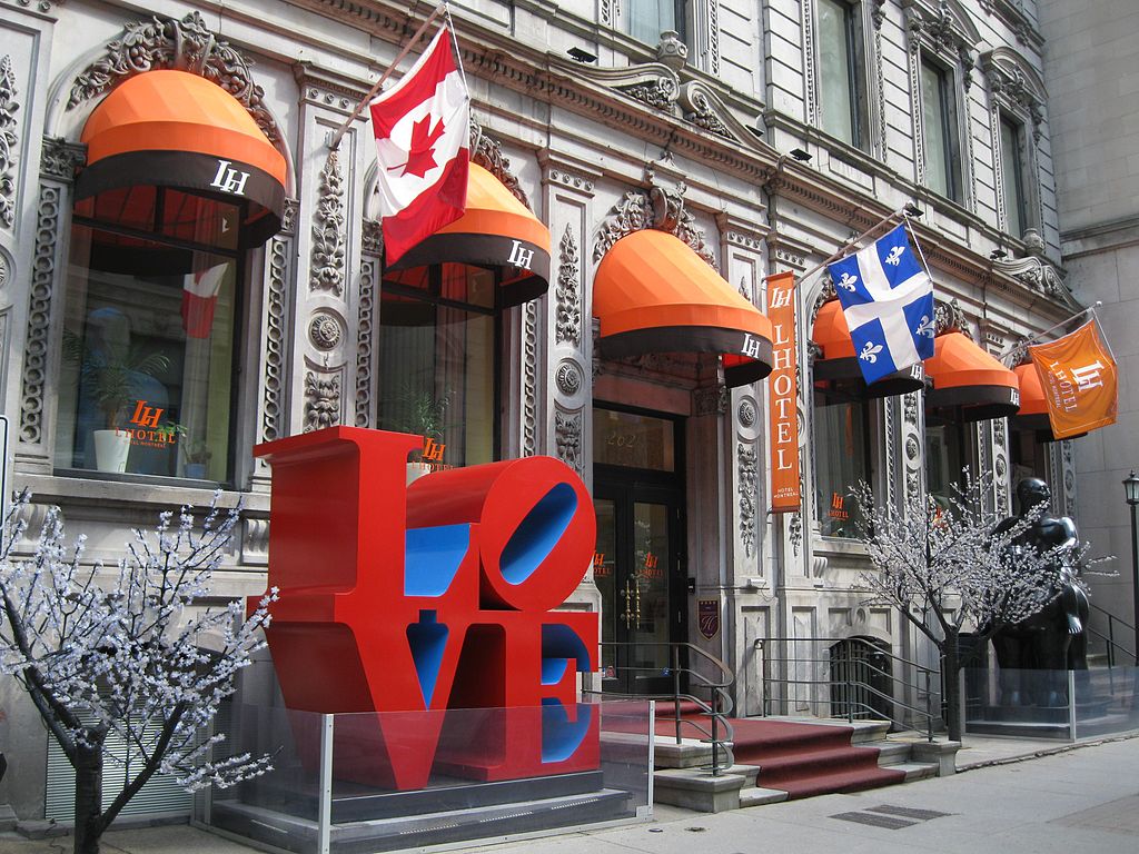 Photo of exterior of LHotel Montreal showing orange awnings, flags and a big LOVE sculpture composed of letters